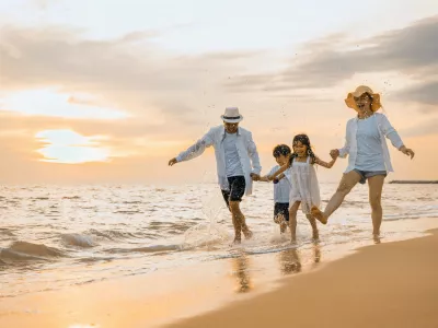 People of father, mother, children son and daughter family of four holding hands together walking outdoor, Happy family having fun running on a sandy beach at sunset, tropical summer travel vacations