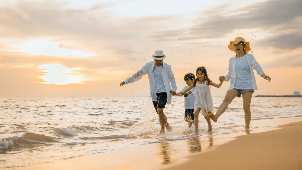 People of father, mother, children son and daughter family of four holding hands together walking outdoor, Happy family having fun running on a sandy beach at sunset, tropical summer travel vacations