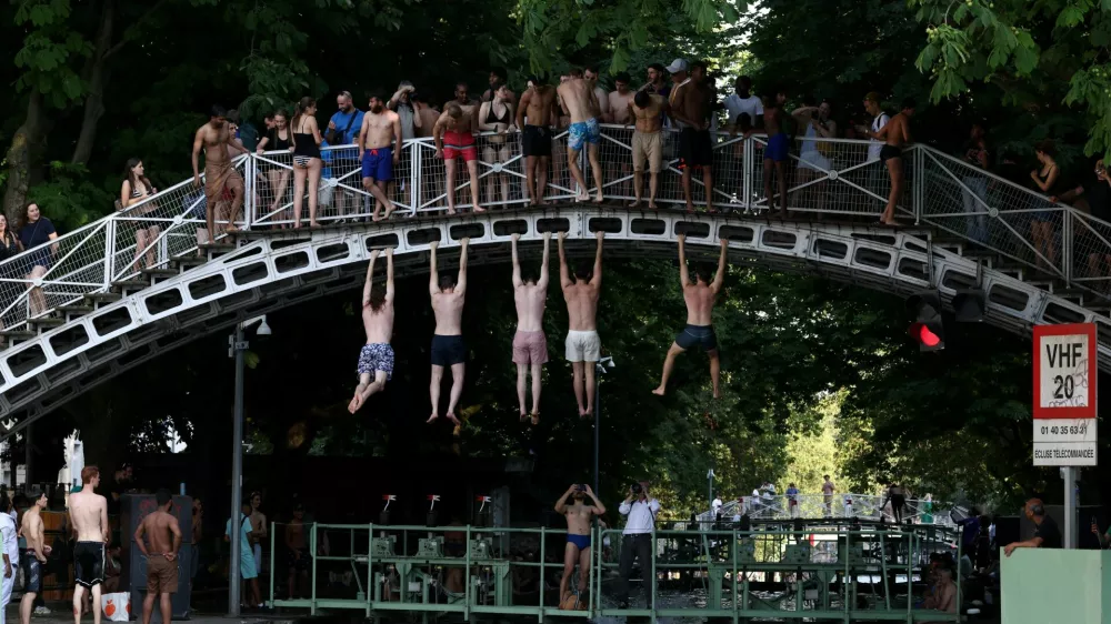 People hang from a bridge above the Canal Saint-Martin after public swimming was permitted in certain areas due to high temperatures amid a heatwave in Paris, France, June 26, 2026. REUTERS/Tom Nicholson   TPX IMAGES OF THE DAY / Foto: Tom Nicholson