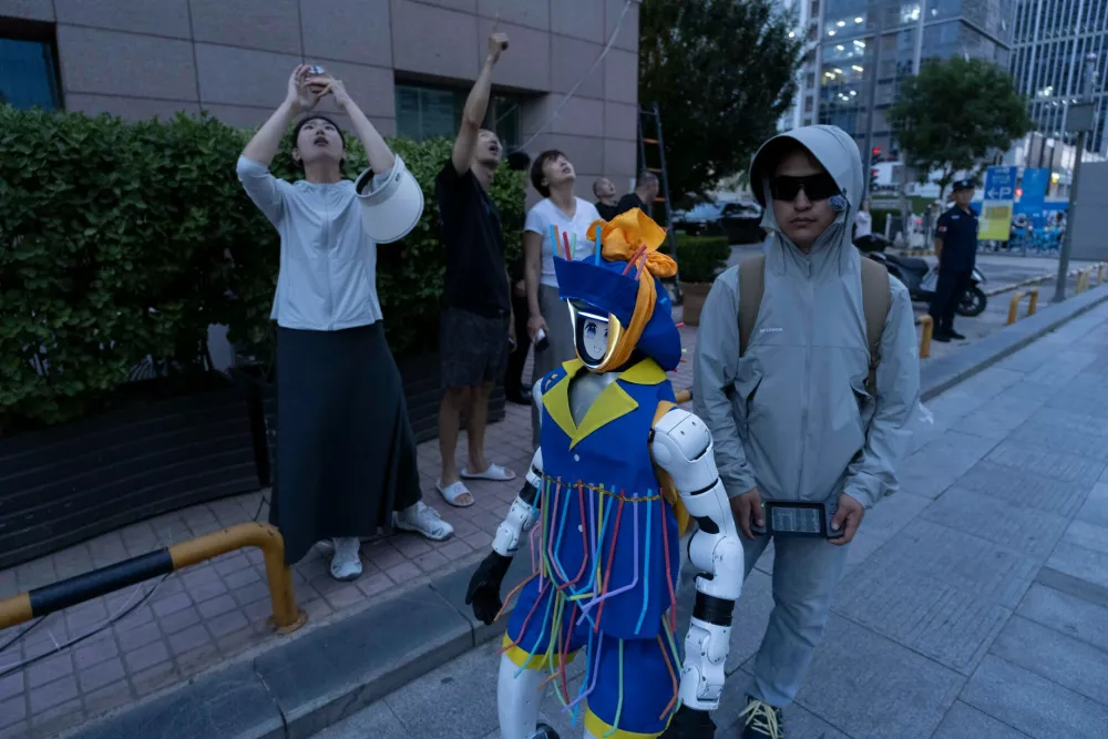 A man remote controls a robot on the street as other passerby look up at the Citic Tower also known as Zun Tower which is damaged in Beijing, China, Friday, June 26, 2026. (AP Photo/Han Guan Ng) 