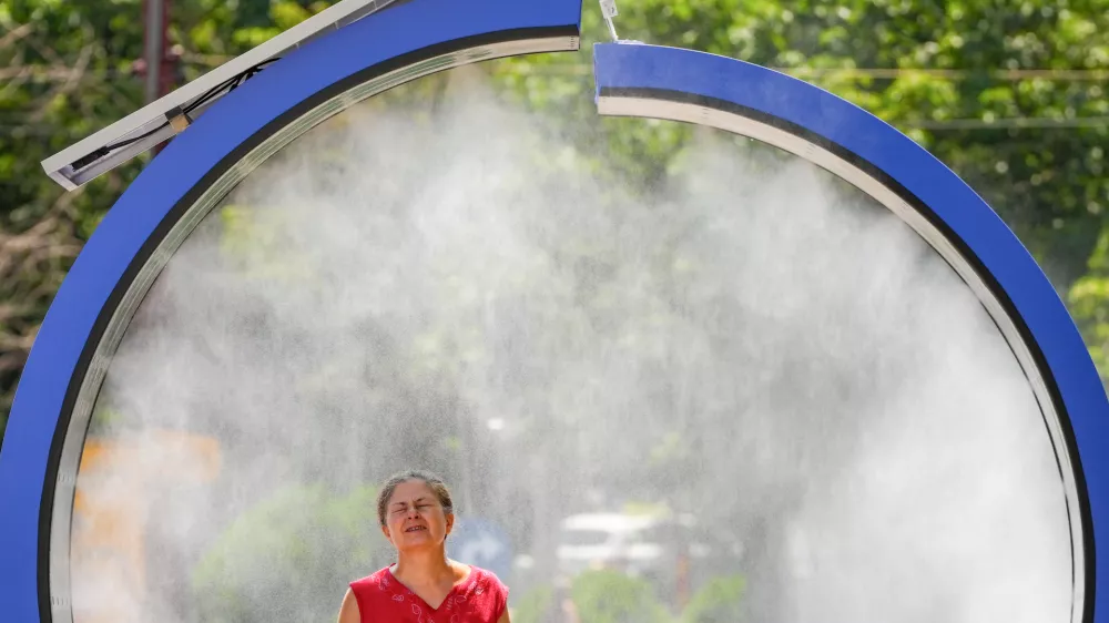 A woman cools off in a water mist machine installed by city administration to assist people in coping with the heat on a torrid day, as the National Weather forecaster issued an extreme heat code red warning for most parts of the country, in Bucharest, Romania, Monday, June 29, 2026. (AP Photo/Vadim Ghirda)