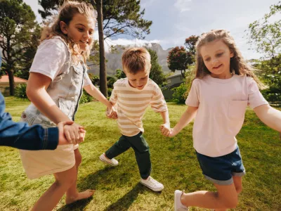 A group of happy children holding hands and playing on a sunny day in a park, enjoying outdoor activities and showcasing friendship, joy, and togetherness in a vibrant and lively environment.