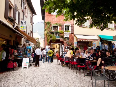 "Malcesine, Italy - April 29, 2012: Lot of people sitting in the cafe drinking and talking. Few people standing and shoping at the town sqare"