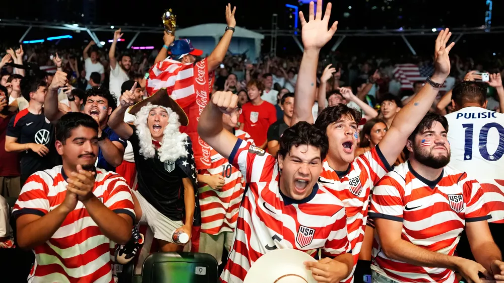 U.S. soccer fans, including Caleb Triana, center, and Nicolas Cerda, dressed as a founding father, celebrate the U.S. scoring its second goal, as they watch a live broadcast of the World Cup round of 32 soccer match between the United States and Bosnia, Wednesday, July 1, 2026, at an official fan fest in downtown Miami. (AP Photo/Rebecca Blackwell)