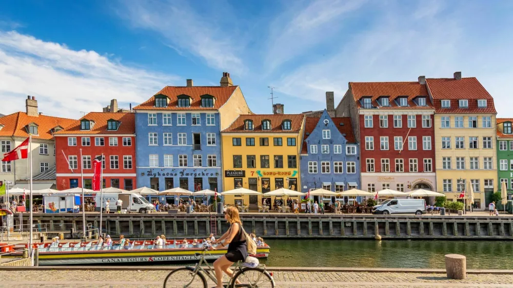 Copenhagen, Denmark - July, 2019: Copenhagen iconic view. Famous old Nyhavn port with colorful medieval houses, tourist ship and woman on a bicycle in the center of Copenhagen. Selective focus.