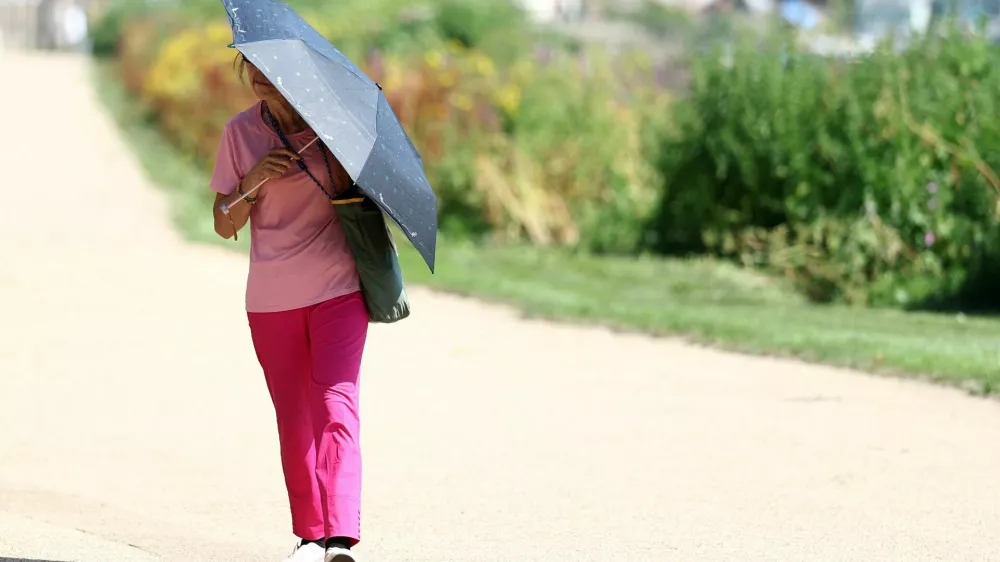 A person uses an umbrella to shield from the sun whilst walking along the River Thames, as Britain experiences record temperatures disrupting schools and transport networks, at Richmond, in London, Britain, June 25, 2026. REUTERS/Toby Melville