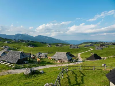 Grazing cows between charming wooden shepherds' huts on scenic mountain plateau. Breath-taking sight of tourist destination with authentic herdsmen's village in alpine landscape on sunny spring day. / Foto: Helivideo