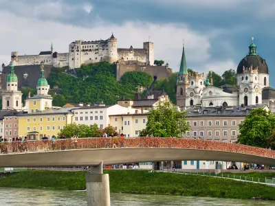 SALZBURG, AUSTRIA - May 4th, 2018: View to Hohensalzburg Fortress and Staatsbruecke bridge across Salzach river on a spring evening with many people walking