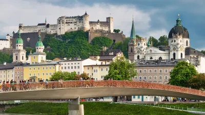 SALZBURG, AUSTRIA - May 4th, 2018: View to Hohensalzburg Fortress and Staatsbruecke bridge across Salzach river on a spring evening with many people walking