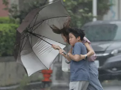 People struggle with umbrella in a rain caused by Typhoon Bavi in Taichung, Taiwan, Saturday, July 11, 2026. (AP Photo/Chiang Ying-ying)