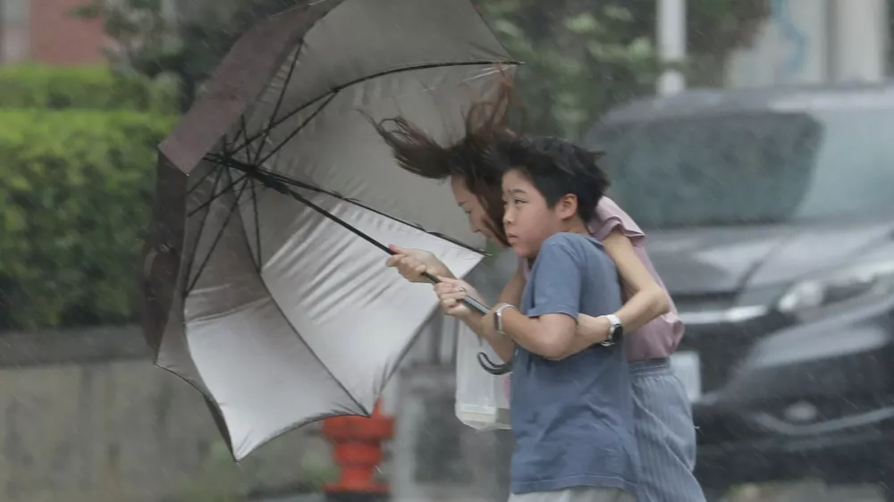 People struggle with umbrella in a rain caused by Typhoon Bavi in Taichung, Taiwan, Saturday, July 11, 2026. (AP Photo/Chiang Ying-ying)