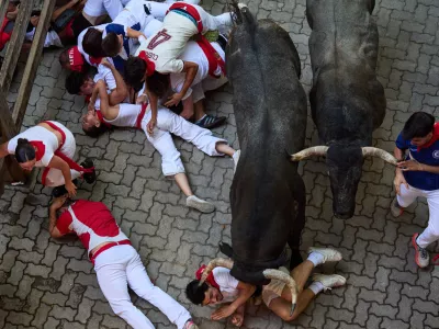 Revelers fall next to Jose Escolar's fighting bulls during the fifth running of the bulls at the San Ferm&iacute;n festival in Pamplona, Spain, Saturday, July 11, 2026. (AP Photo/Miguel Oses)