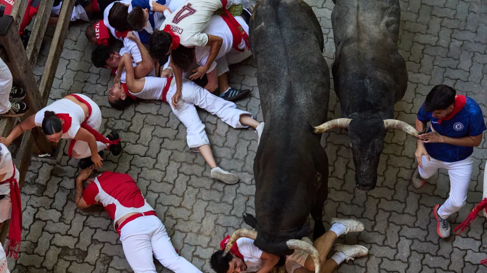 Revelers fall next to Jose Escolar's fighting bulls during the fifth running of the bulls at the San Ferm&iacute;n festival in Pamplona, Spain, Saturday, July 11, 2026. (AP Photo/Miguel Oses)