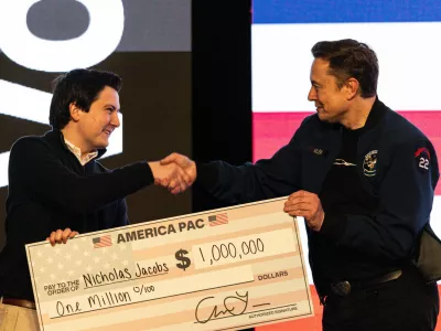 FILE - Elon Musk hands over a million dollar check to Nicholas Jacobs during a town hall in Green Bay, Wis., March 30, 2025. (AP Photo/Jeffrey Phelps, File)