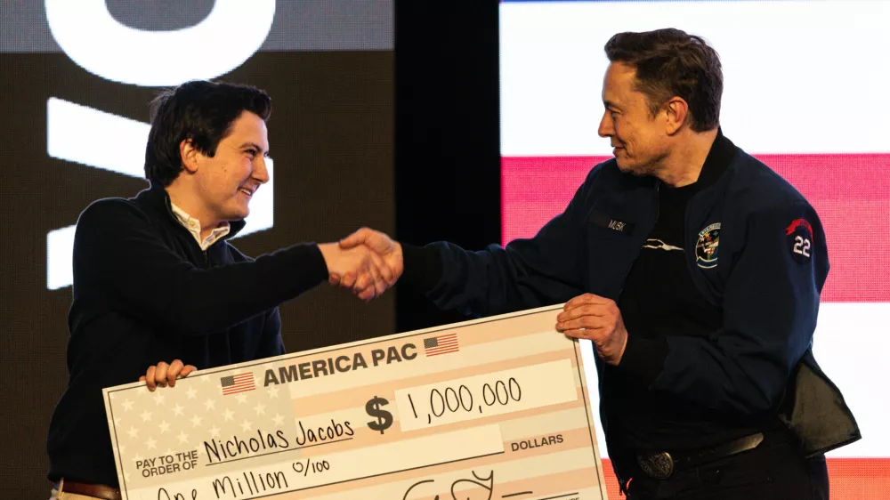 FILE - Elon Musk hands over a million dollar check to Nicholas Jacobs during a town hall in Green Bay, Wis., March 30, 2025. (AP Photo/Jeffrey Phelps, File)