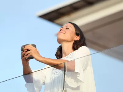 Adult woman with coffee cup breathing on a balcony / Foto: Pheelings Media Getty Images