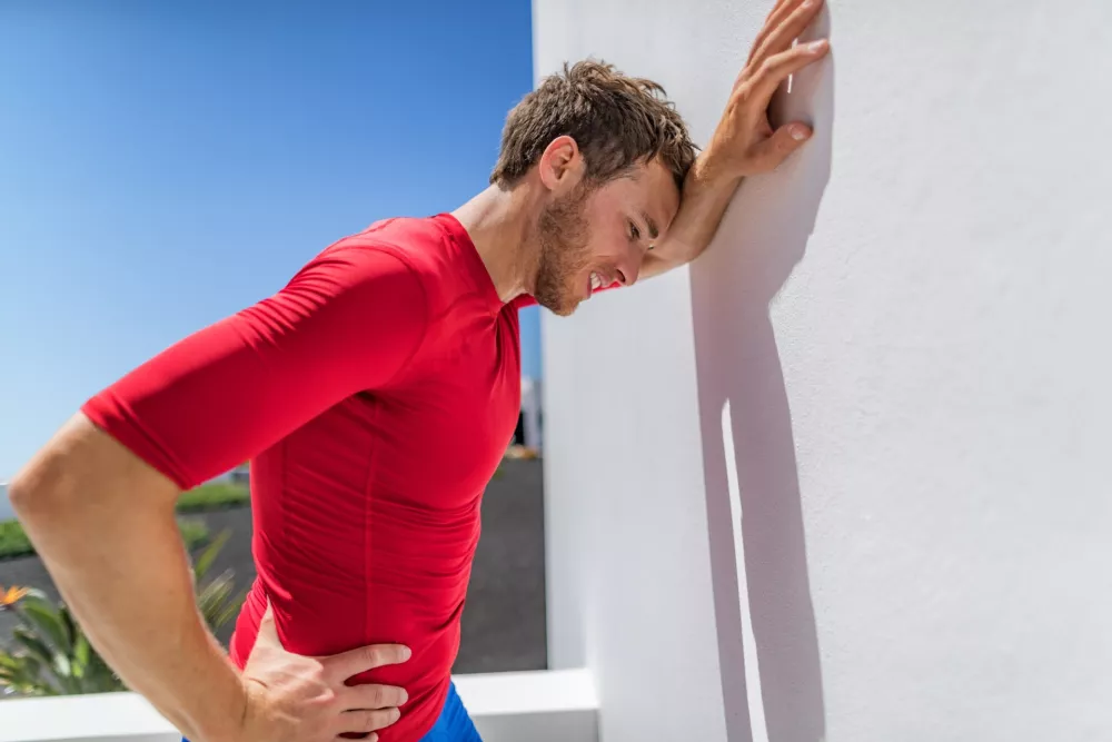 Tired athlete runner man exhausted leaning on wall of fatigue breathing hard after difficult exercise. Fitness person sweating of sun stroke, migraine, heat exhaustion muscle back pain or cramps. / Foto: Maridav
