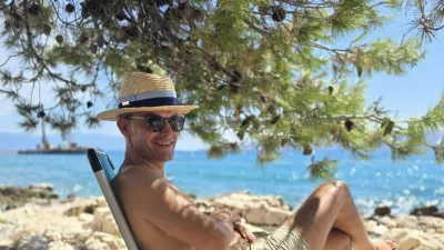 Anže Logar na plaži pod borovci s klobukom, ki ga &scaron;čiti pred močnim soncem. 