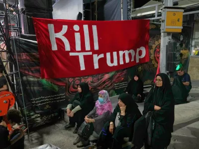 Women sit beneath a banner reading in English, "Kill Trump," during a pro-government rally in Tehran, Friday, July 17, 2026. (AP Photo/Vahid Salemi)
