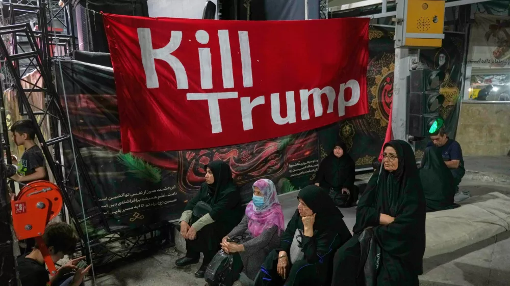 Women sit beneath a banner reading in English, "Kill Trump," during a pro-government rally in Tehran, Friday, July 17, 2026. (AP Photo/Vahid Salemi)