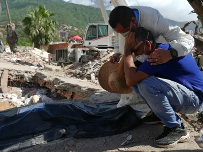 A Catholic priest comforts Carlos Berroter&aacute;n beside the body of his niece, Manuela Sol&oacute;rzano, 17, recovered from the rubble of their home three weeks after it collapsed during the earthquakes that struck La Guaira, Venezuela, Friday, July 17, 2026. (AP Photo/Ariana Cubillos)
