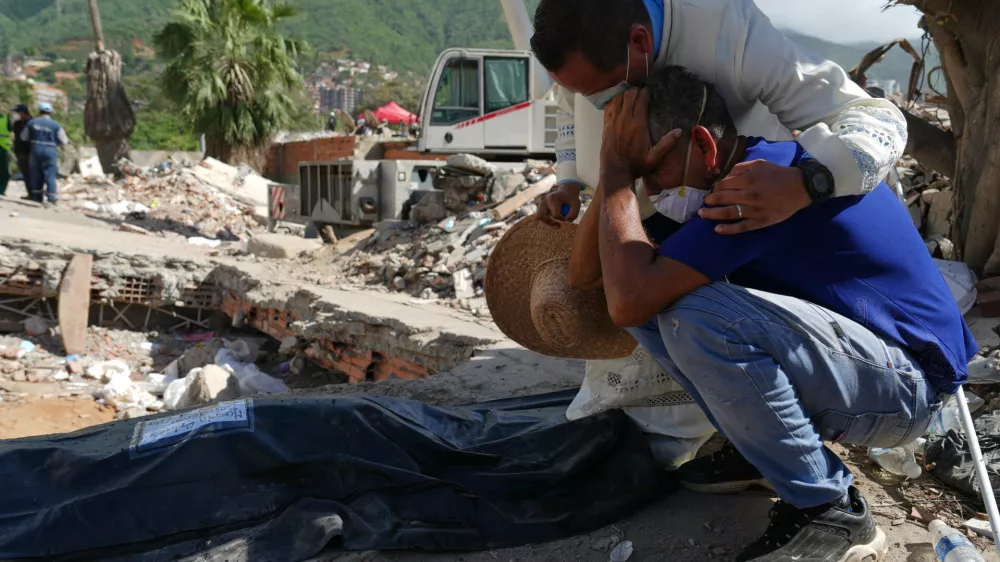 A Catholic priest comforts Carlos Berroter&aacute;n beside the body of his niece, Manuela Sol&oacute;rzano, 17, recovered from the rubble of their home three weeks after it collapsed during the earthquakes that struck La Guaira, Venezuela, Friday, July 17, 2026. (AP Photo/Ariana Cubillos)