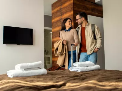 Smiling couple with suitcase arriving in hotel room.