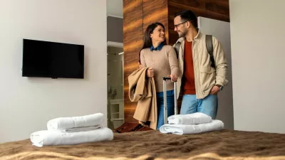 Smiling couple with suitcase arriving in hotel room.