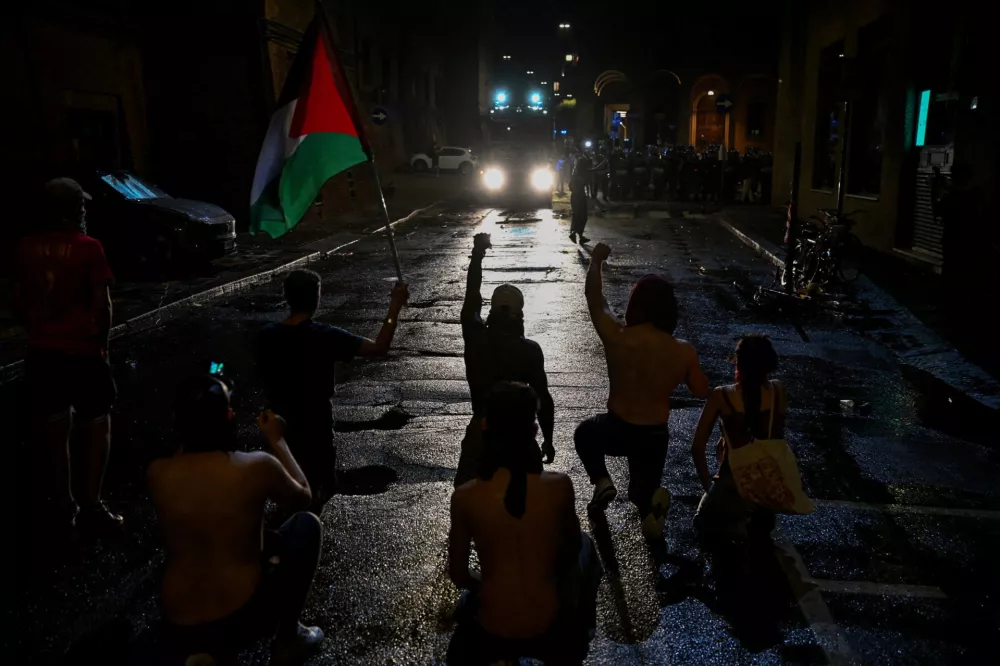 Protesters kneel and raise their fists while facing a police line during a demonstration following the death of Abderrahim Fakir, in Bologna, Italy, July 20, 2026. REUTERS/Michele Lapini  TPX IMAGES OF THE DAY