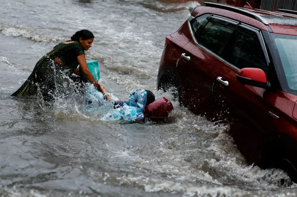 A commuter helps another woman after she falls due to the force of floodwaters while wading through a waterlogged street following torrential rain in Ahmedabad, India, July 23, 2026. REUTERS/Amit Dave   TPX IMAGES OF THE DAY