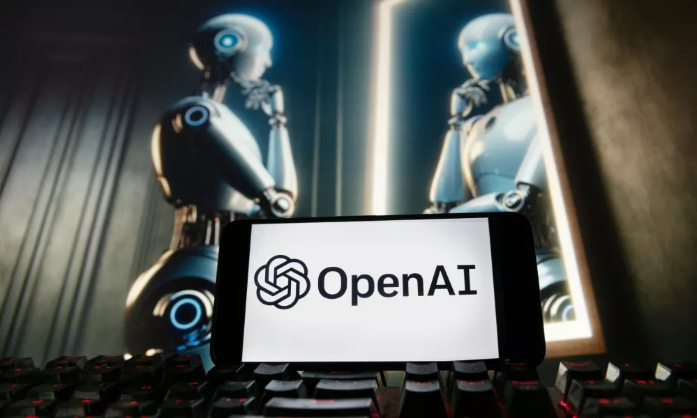 FILE - The OpenAI logo is displayed on a cellphone with an image on a computer monitor generated by ChatGPT's Dall-E text-to-image model, Dec. 8, 2023, in Boston. (AP Photo/Michael Dwyer, File)