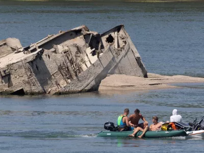 People in a boat pass by a sunken German warship from World War II, exposed due to low Danube River levels caused by drought and extreme heat, in Prahovo, Serbia, July 30, 2026. REUTERS/Djordje Kojadinovic