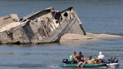 People in a boat pass by a sunken German warship from World War II, exposed due to low Danube River levels caused by drought and extreme heat, in Prahovo, Serbia, July 30, 2026. REUTERS/Djordje Kojadinovic