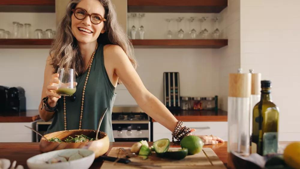 Healthy senior woman smiling while holding some green juice in her kitchen. Mature woman serving herself wholesome vegan food at home. Happy woman taking care of her aging body with a plant-based diet. / Foto: Jacoblund Getty Images