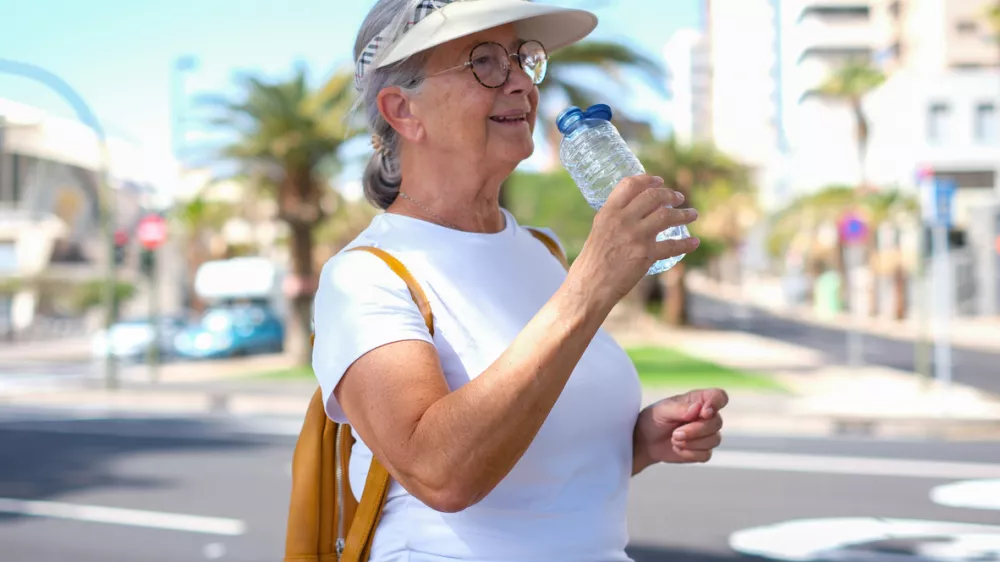 Active elderly tourist woman casual dressed drinks from a bottle water along the urban street, city life in background / Foto: Lucigerma Getty Images