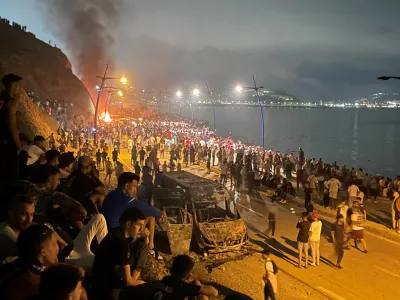 Migrants gather around a torched vehicle while waiting for a chance to cross to the Spanish enclave of Ceuta, on the Moroccan side of the border in Fnideq, Morocco, July 31, 2026. Picture taken with a mobile phone.  REUTERS/Ahmed El Jechtimi