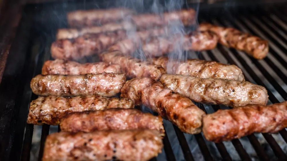 Grilling Meat on barbecue grill with hot coal. Preparing, cooking cevapcici, kebabs, country sausage on charcoal barbecue BBQ in outside fireplace. Traditional Turkish, Bosnian, Serbian, Croatian food