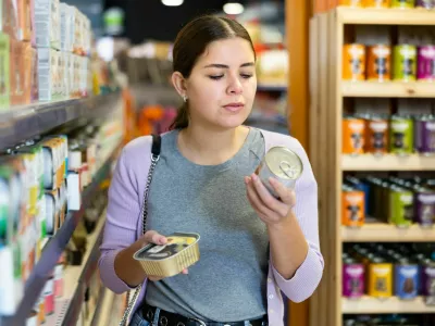 Positive young woman choosing canned natural nutritious dog food for her pet in store / Foto: Jackf