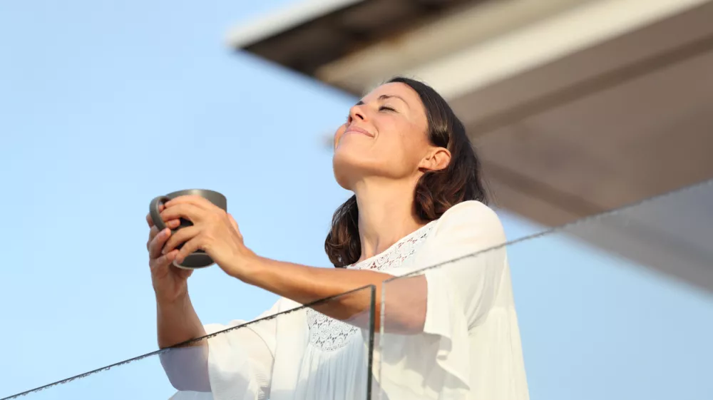 Adult woman with coffee cup breathing on a balcony