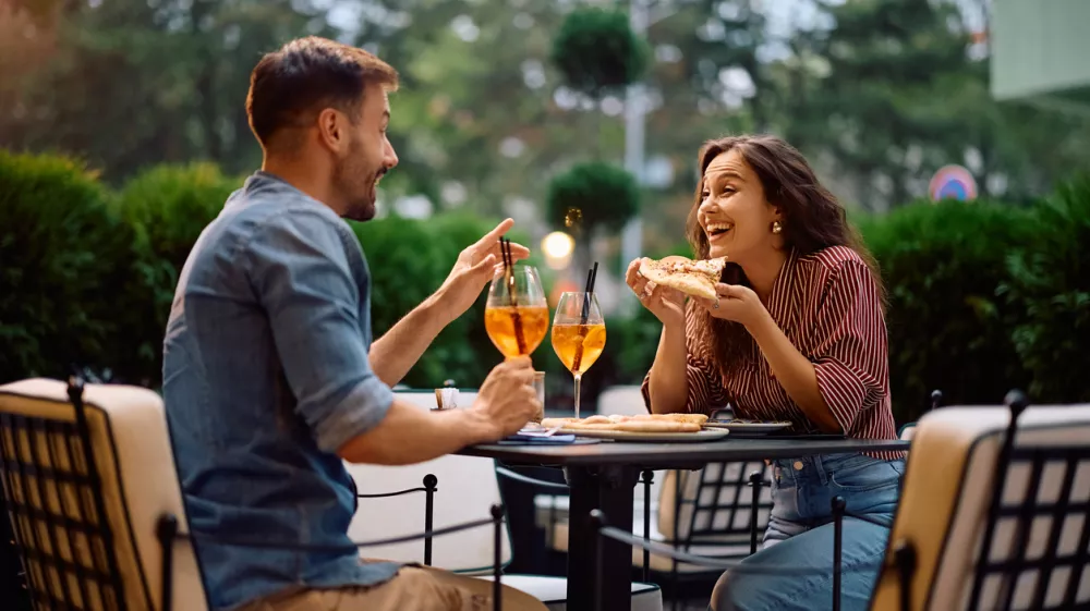 Young happy couple communicating while eating pizza in restaurant.