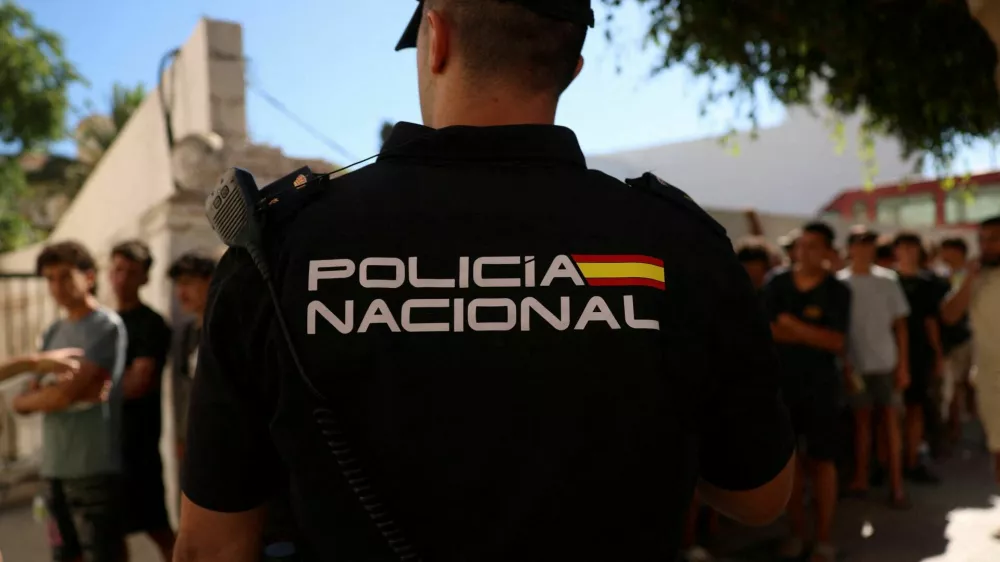 A police officer stands guard as migrant children queue outside a police station to be registered following mass crossings by migrants on foot and by sea from Morocco into Spanish territory, in Ceuta, Spain, August 6, 2026. REUTERS/Violeta Santos Moura   TPX IMAGES OF THE DAY