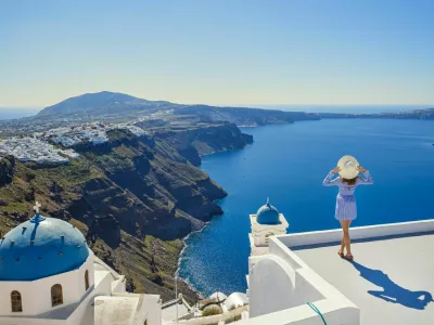 Young woman stands on a hill and looks at the marine landscape of Santorini, Greece