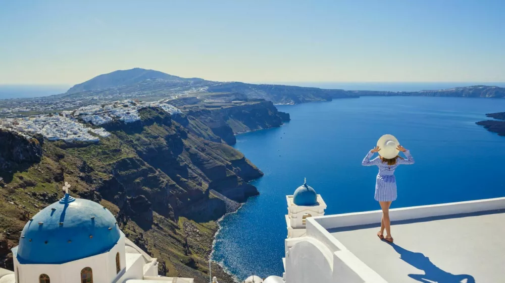 Young woman stands on a hill and looks at the marine landscape of Santorini, Greece