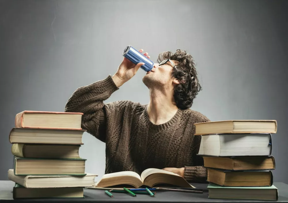 Young man drinking energy drink while studying. College student concept. Energizing before learning. / Foto: Niserin