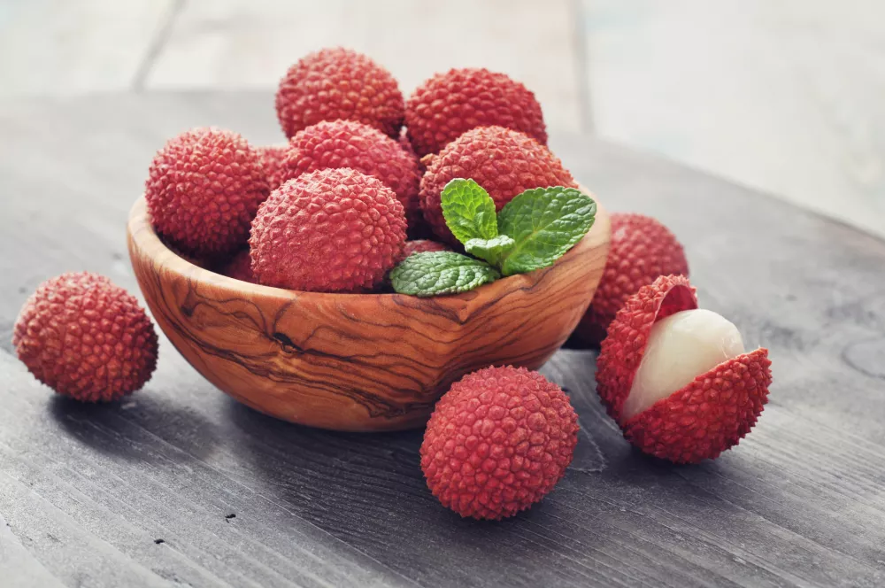 Fresh lychee in bowl on a wooden background / Foto: Tashka2000