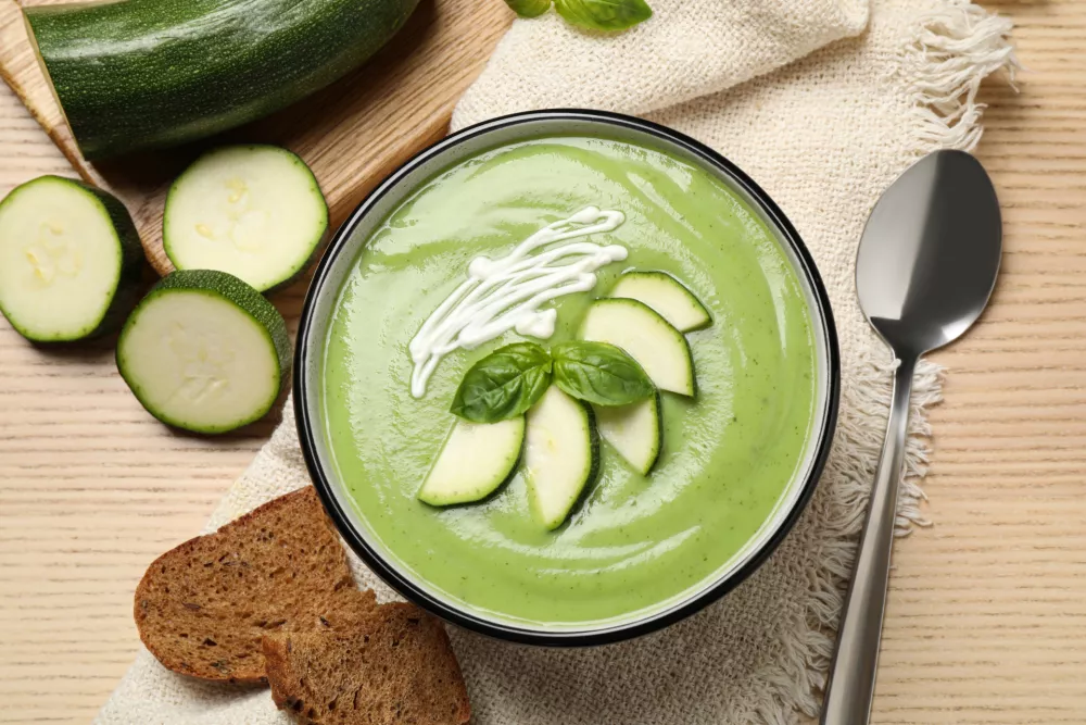 Tasty homemade zucchini cream soup served on wooden table, flat lay / Foto: Liudmila Chernetska