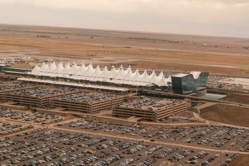 Denver International Airport, Denver, Colorado, USA - October 11, 2023 - Aerial view of the Jeppesen Terminal at Denver International Airport (DEN), Colorado, featuring its distinctive white tent-like roof structures. Surrounding the terminal are expansive parking facilities with multiple levels and numerous cars. The landscape is flat, with open fields in the background. The terminal architecture is designed to resemble the peaks of the nearby Rocky Mountains, creating an iconic silhouette. / Foto: Johnemac72