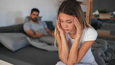 Beautiful depressed woman sitting on bed while her angry boyfriend yells at the background / Foto: Jelena Danilovic