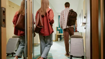 Rear view of young Caucasian couple walking into hotel room with suitcases, arriving for vacation. Image represents hospitality and travel booking, suitable for tourism marketing campaigns / Foto: Annastills