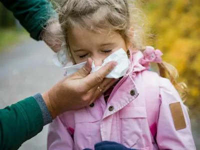Father wiping daughter's nose with handkerchief. Sick little girl with cold and flu standing outdoors. Preschooler sneezing, coughing, having runny red nose. Autumn street background / Foto: Suzi Media Production